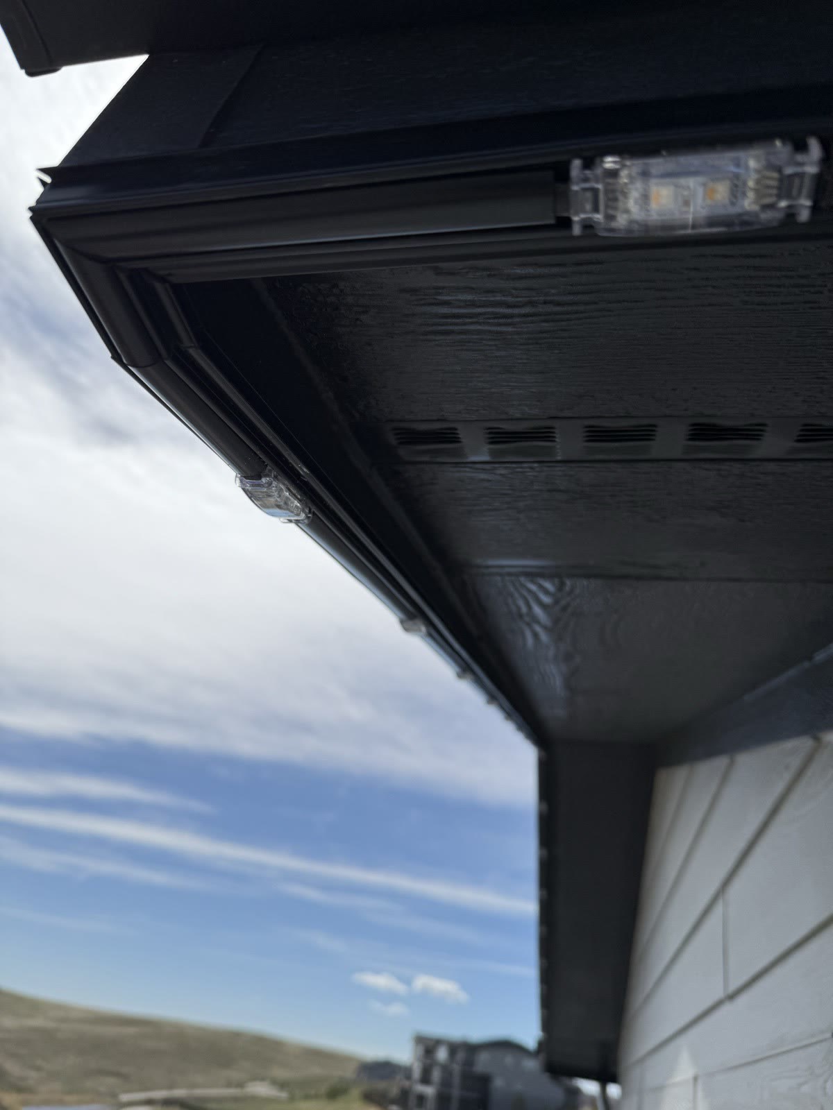 Low-profile black permanent lighting track mounted beneath a home's eaves in daylight